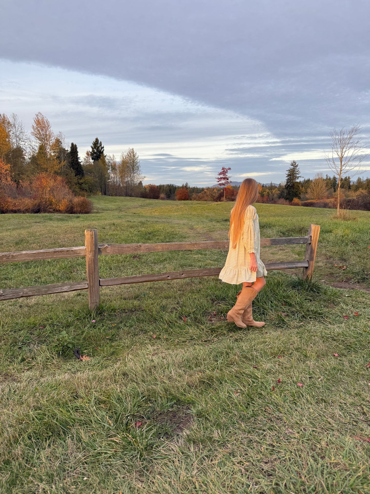 Woman walking in a field with a wooden fence and trees in the background