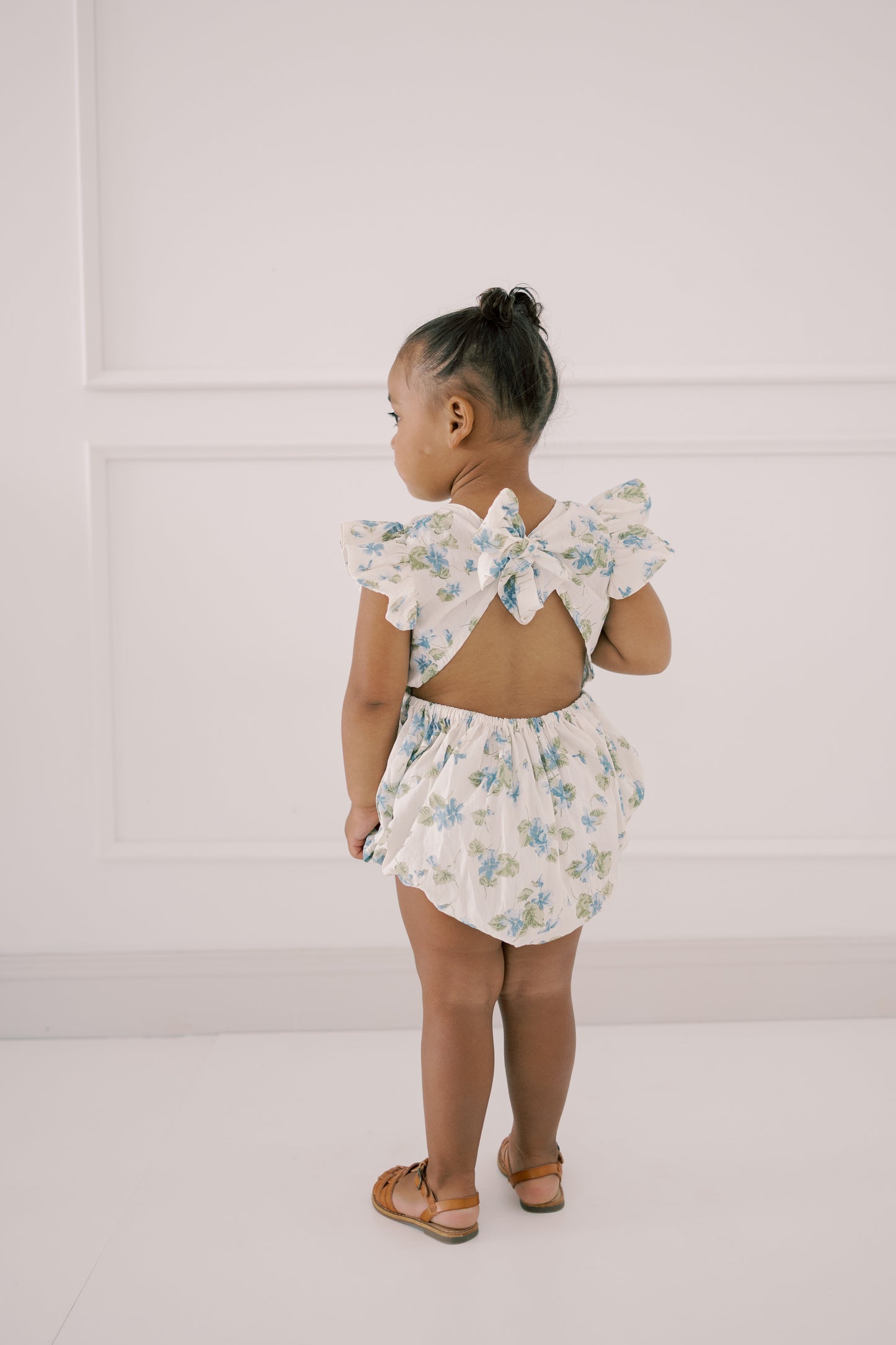 Child wearing a floral romper with tied back bow back closure
