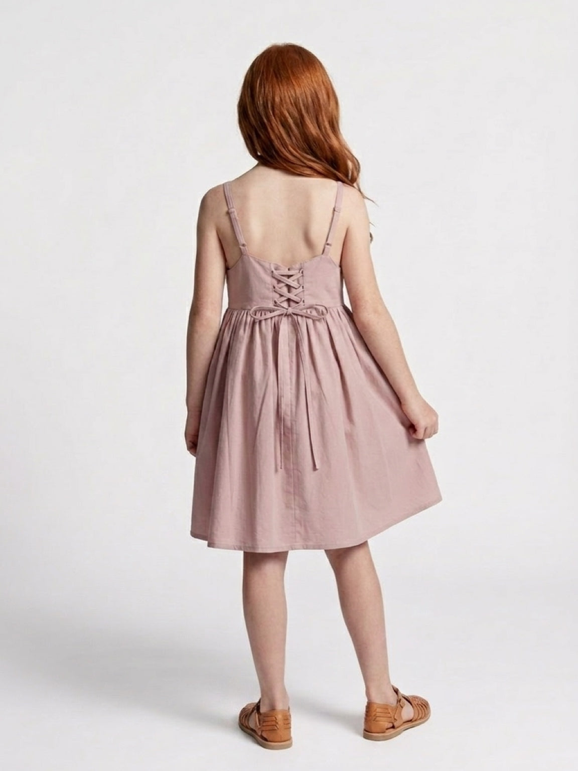 Person wearing a pink dress with a lace-up back on a white background