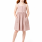 A young girl with red hair stands barefoot against a white studio background, wearing a sleeveless dusty pink dress with a buttoned bodice and front pockets.