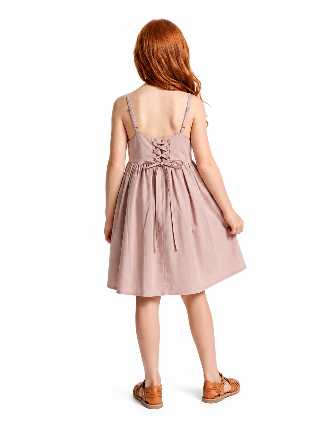 A child model shown from the back wearing a dusty pink sleeveless dress with thin straps, a lace-up back, and a gathered skirt, paired with brown sandals on a white background.