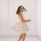 Young girl in a floral dress standing against a white paneled wall.