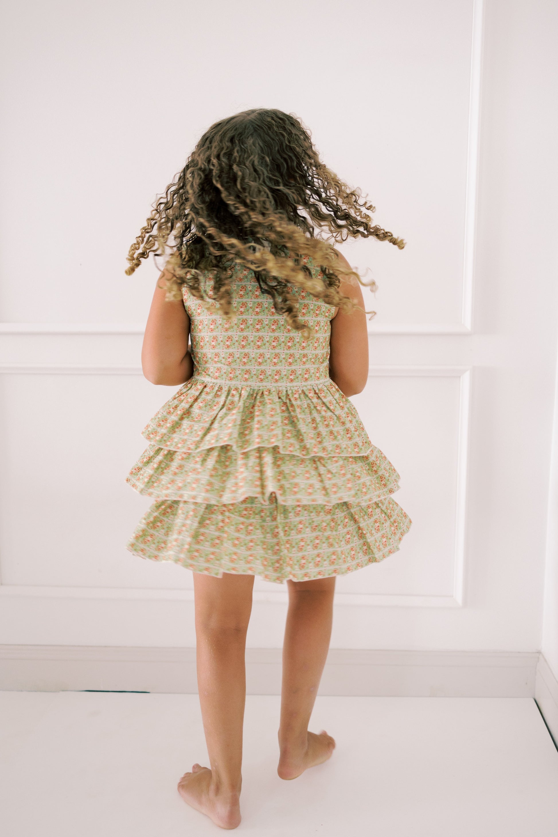 Child wearing a floral dress standing against a white wall