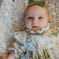Baby in a floral dress with a green bow sitting on a textured surface
