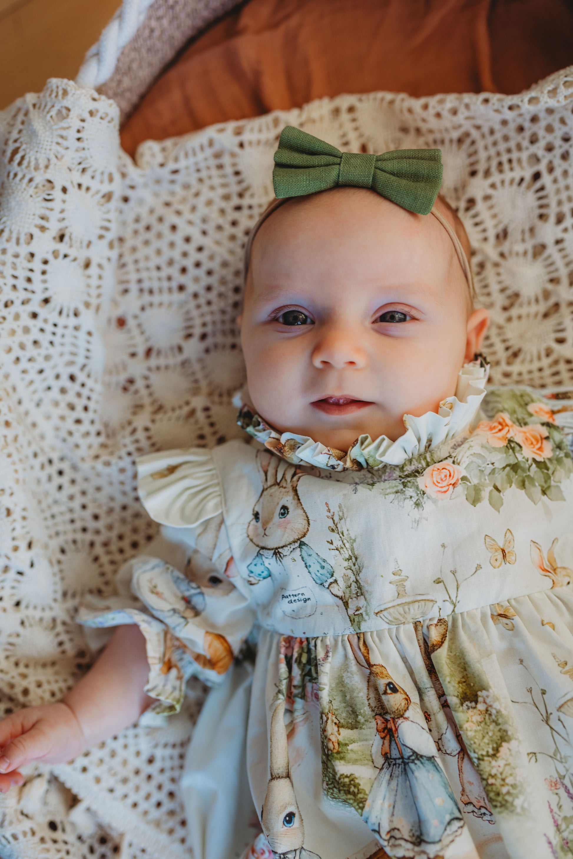 Baby in a floral dress with a green bow sitting on a textured surface