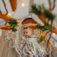 Baby in a decorative setting with pumpkins and lace, likely during Halloween.