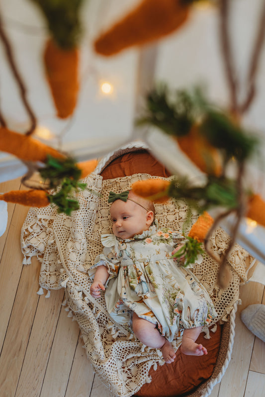 Baby in a decorative setting with pumpkins and lace, likely during Halloween.