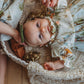 Baby in a floral outfit lying in a woven basket with a soft focus background
