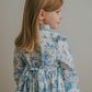 Young girl wearing a blue toile floral dress against a plain background