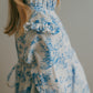 Close-up of a girl wearing a blue toile floral dress with ruffled sleeves.