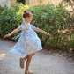 Young girl in a blue floral dress dancing in a park with a classical building in the background