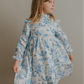 Child wearing a blue toile floral dress against a plain background