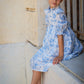 Young girl in a blue floral dress sitting on a step.