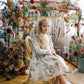 Young girl in a floral dress sitting on a decorated swing surrounded by flowers.