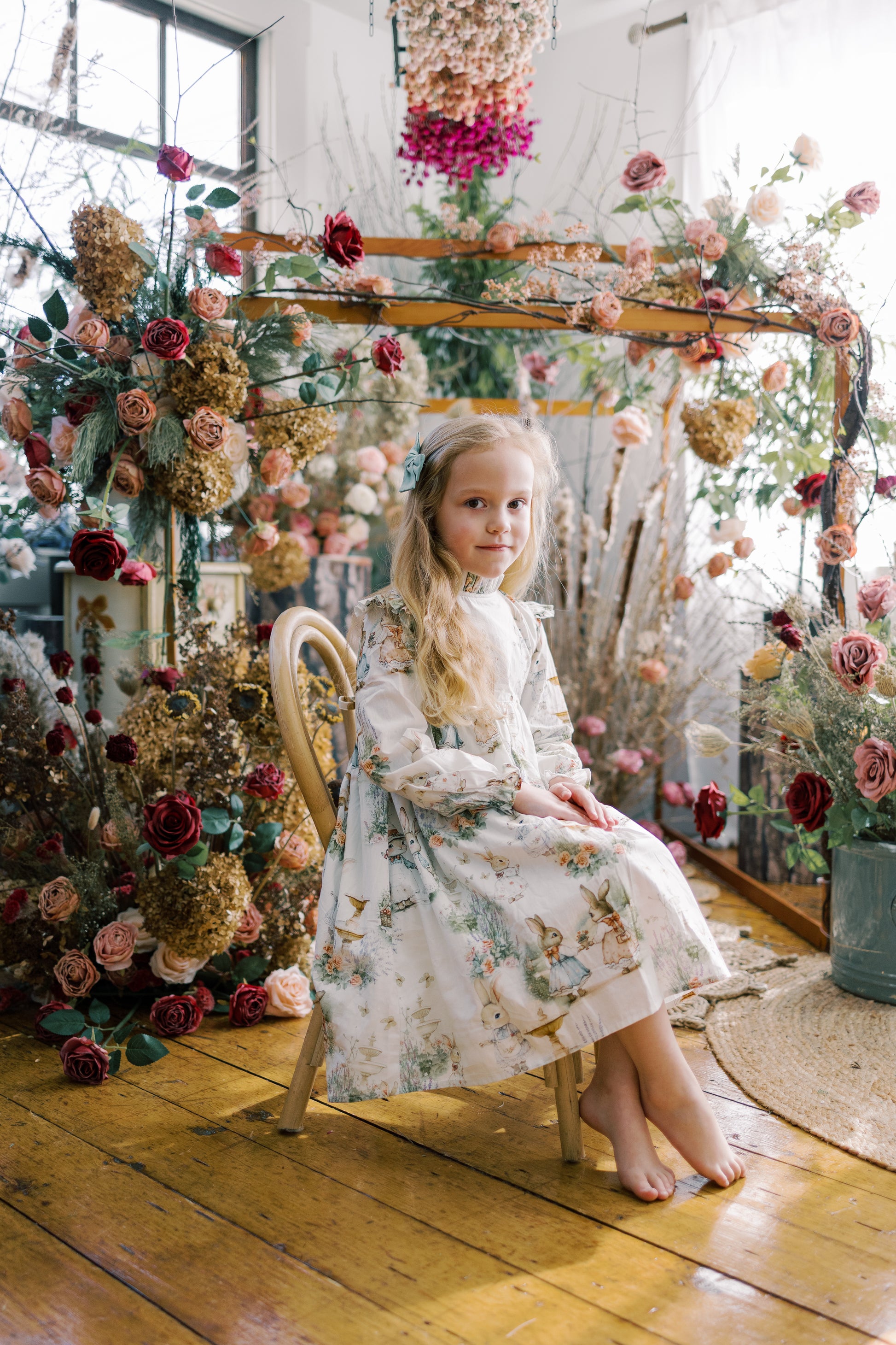 Young girl in a floral dress sitting on a decorated swing surrounded by flowers.