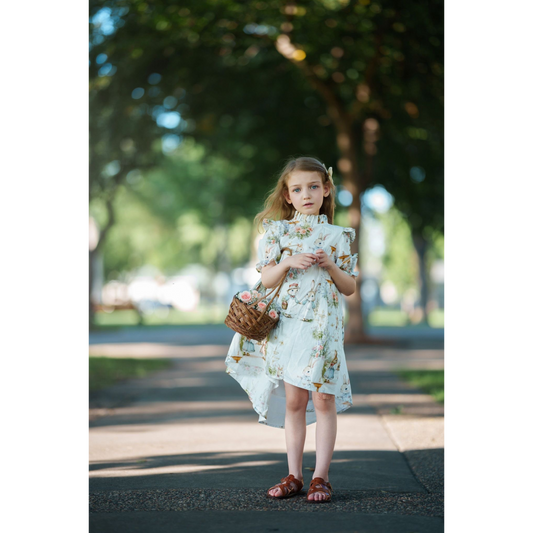 Young girl in a floral dress standing outdoors with trees in the background