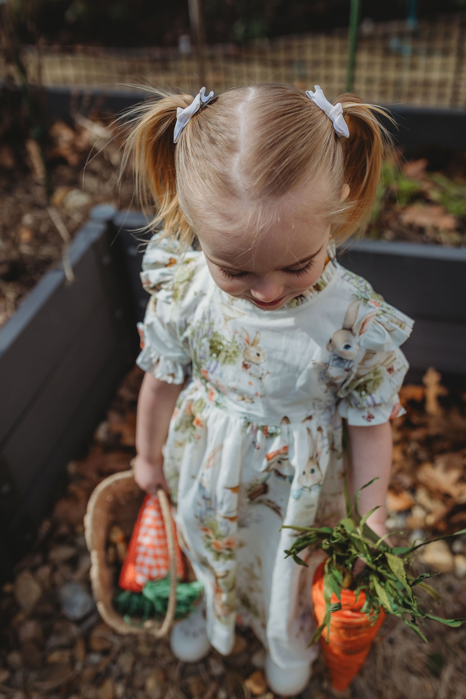 Young girl in a floral dress holding a basket and carrot in an outdoor setting
