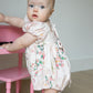Baby in a floral bubble standing next to a pink chair