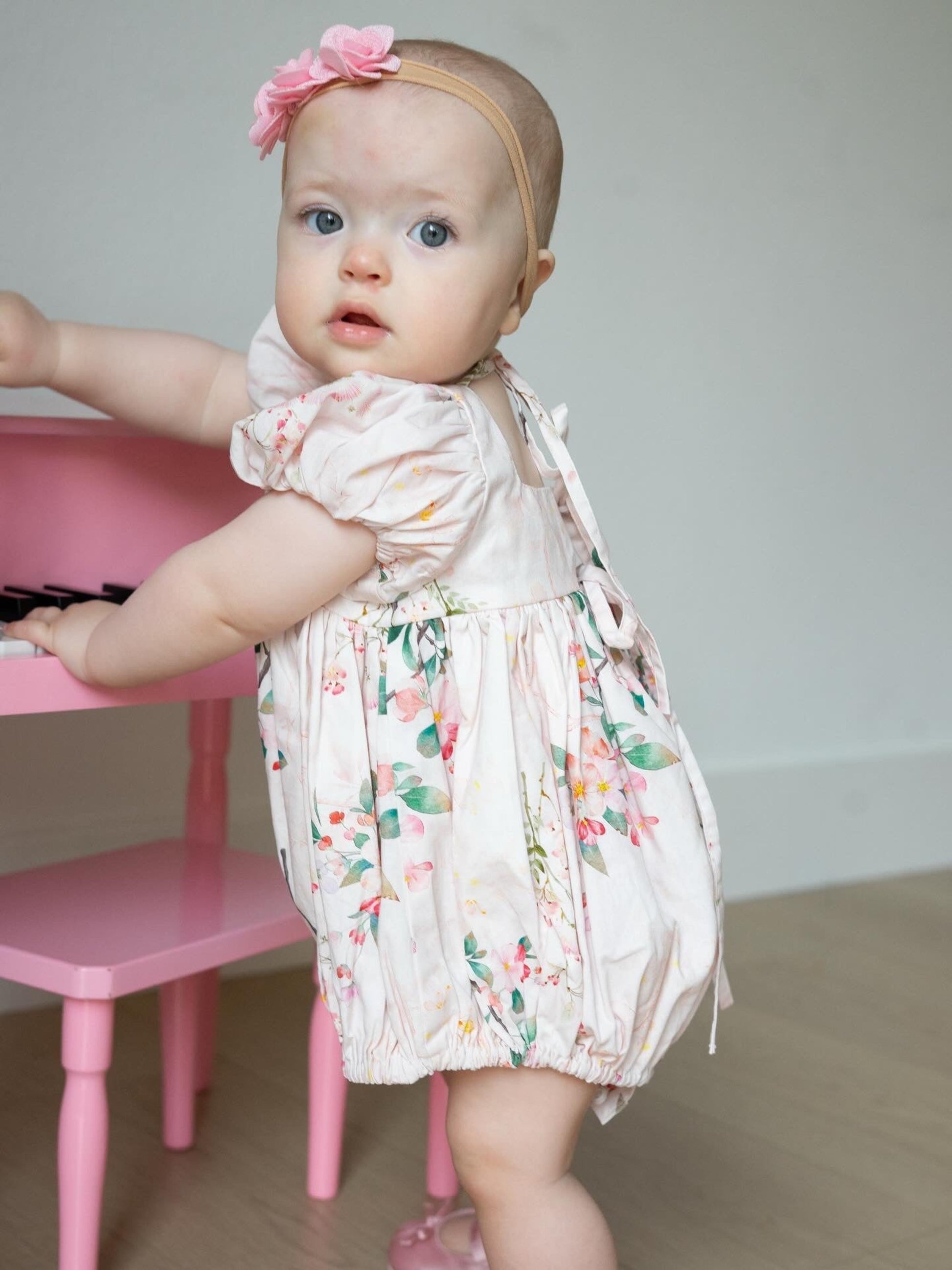 Baby in a floral bubble standing next to a pink chair
