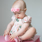 Baby sitting on a pink toy piano with a floral bubble and headband.