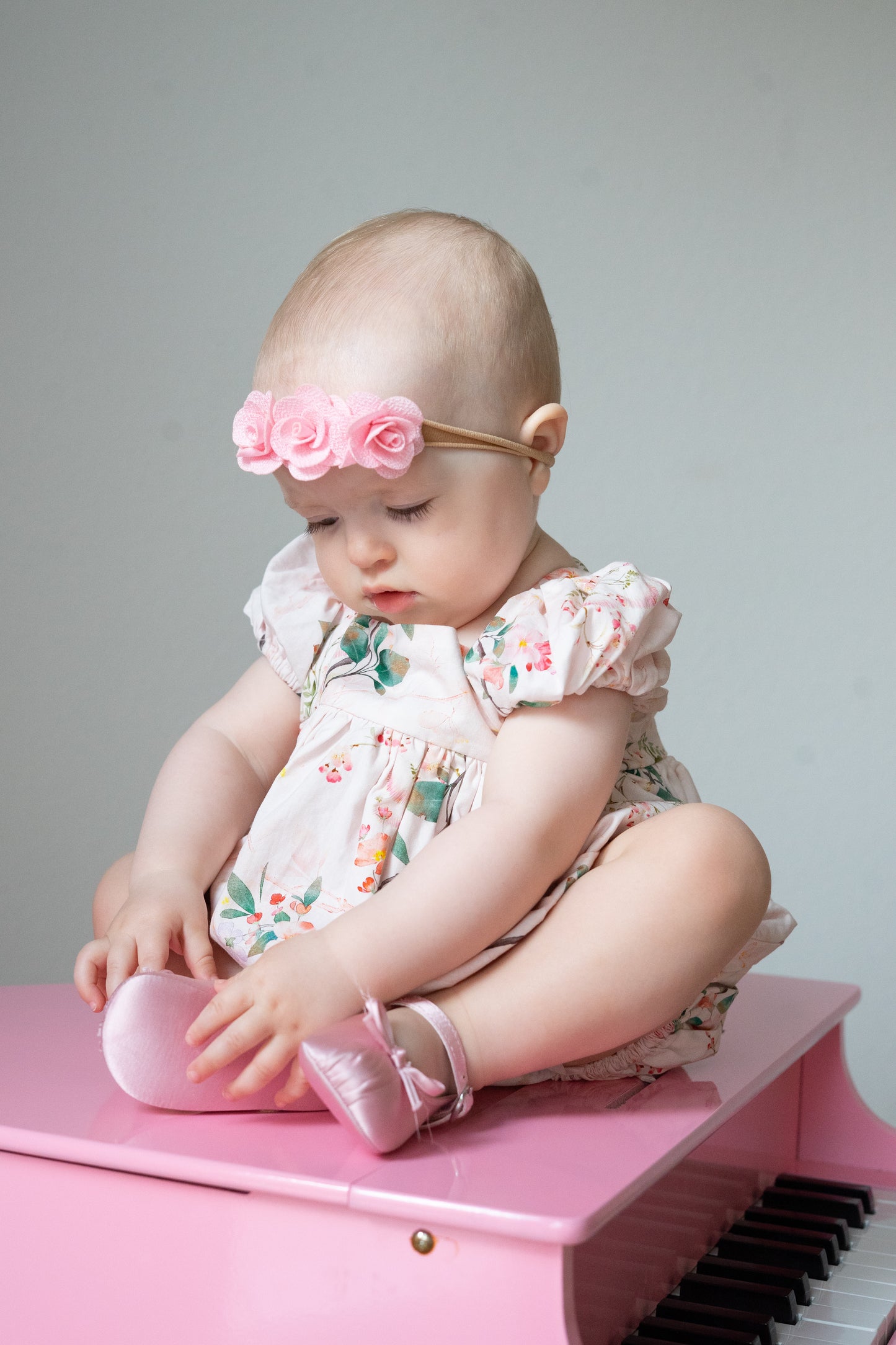 Baby sitting on a pink toy piano with a floral bubble and headband.