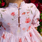 Close-up of a person wearing a floral dress with pink flowers and green leaves against a blurred floral background.