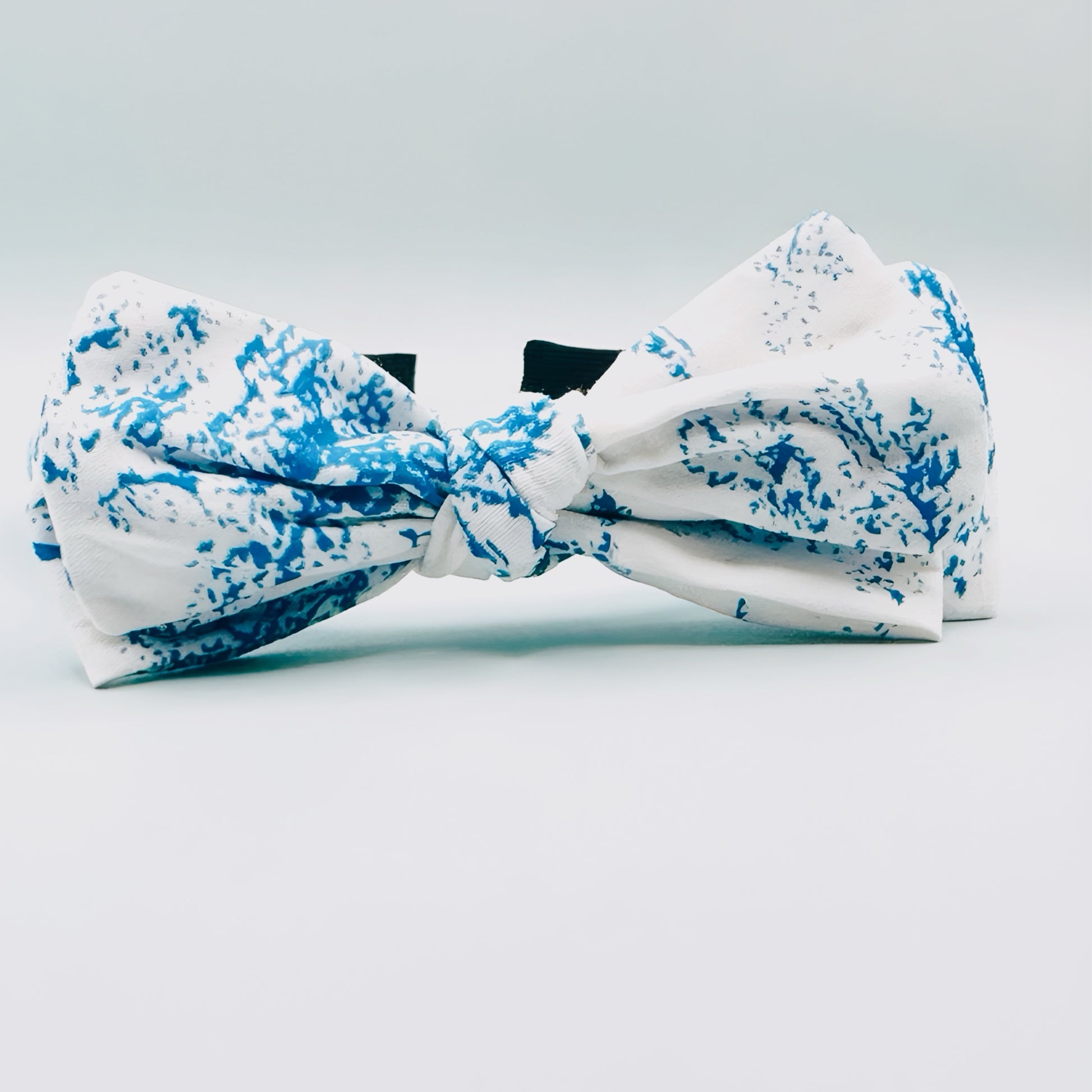 White bow tie with blue splatter pattern on a light gray background