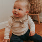 A baby wearing a brown sailor-style collar bib with a knotted tie.