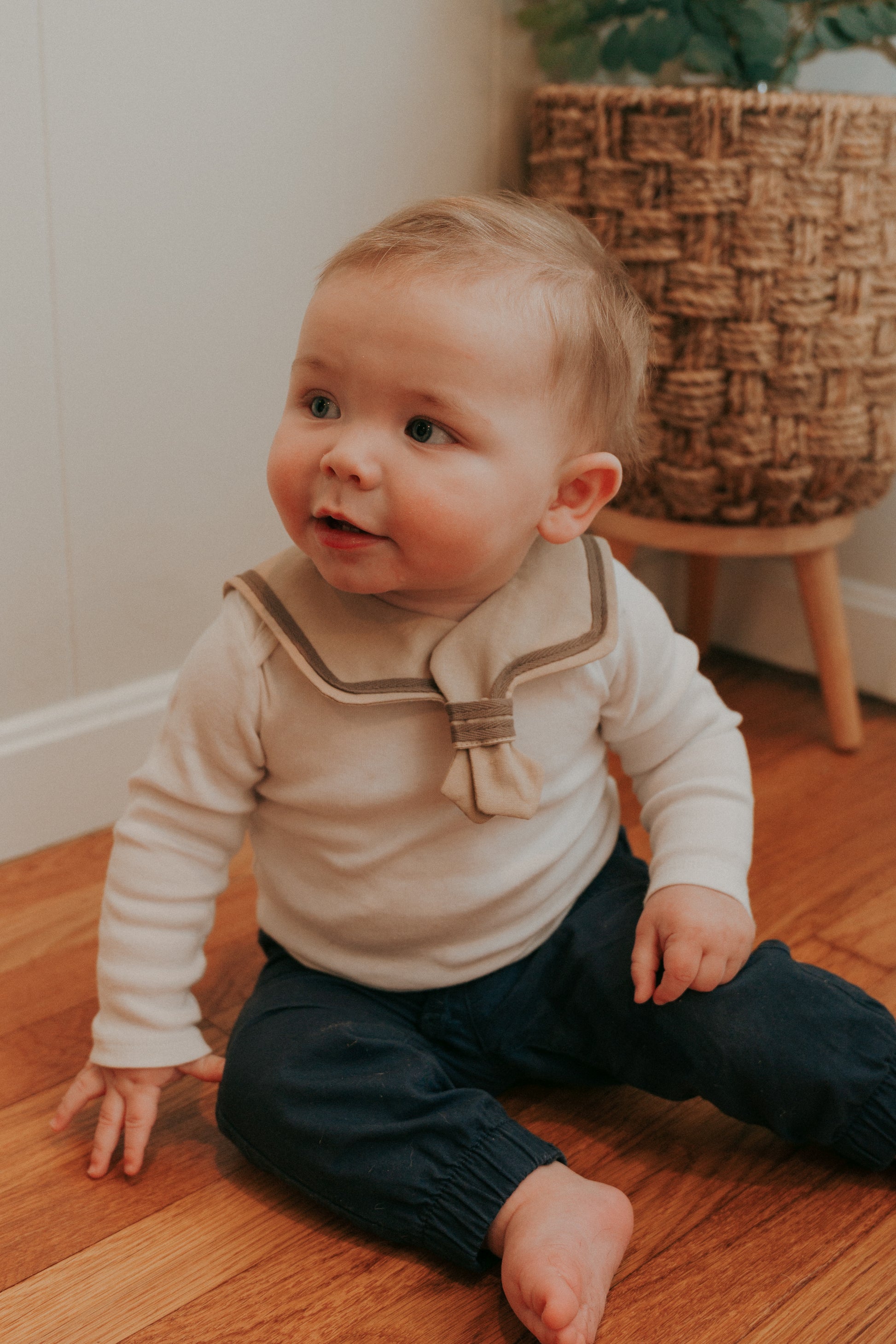 A baby wearing a brown sailor-style collar bib with a knotted tie.