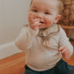 A baby wearing a brown sailor-style collar bib with a knotted tie.