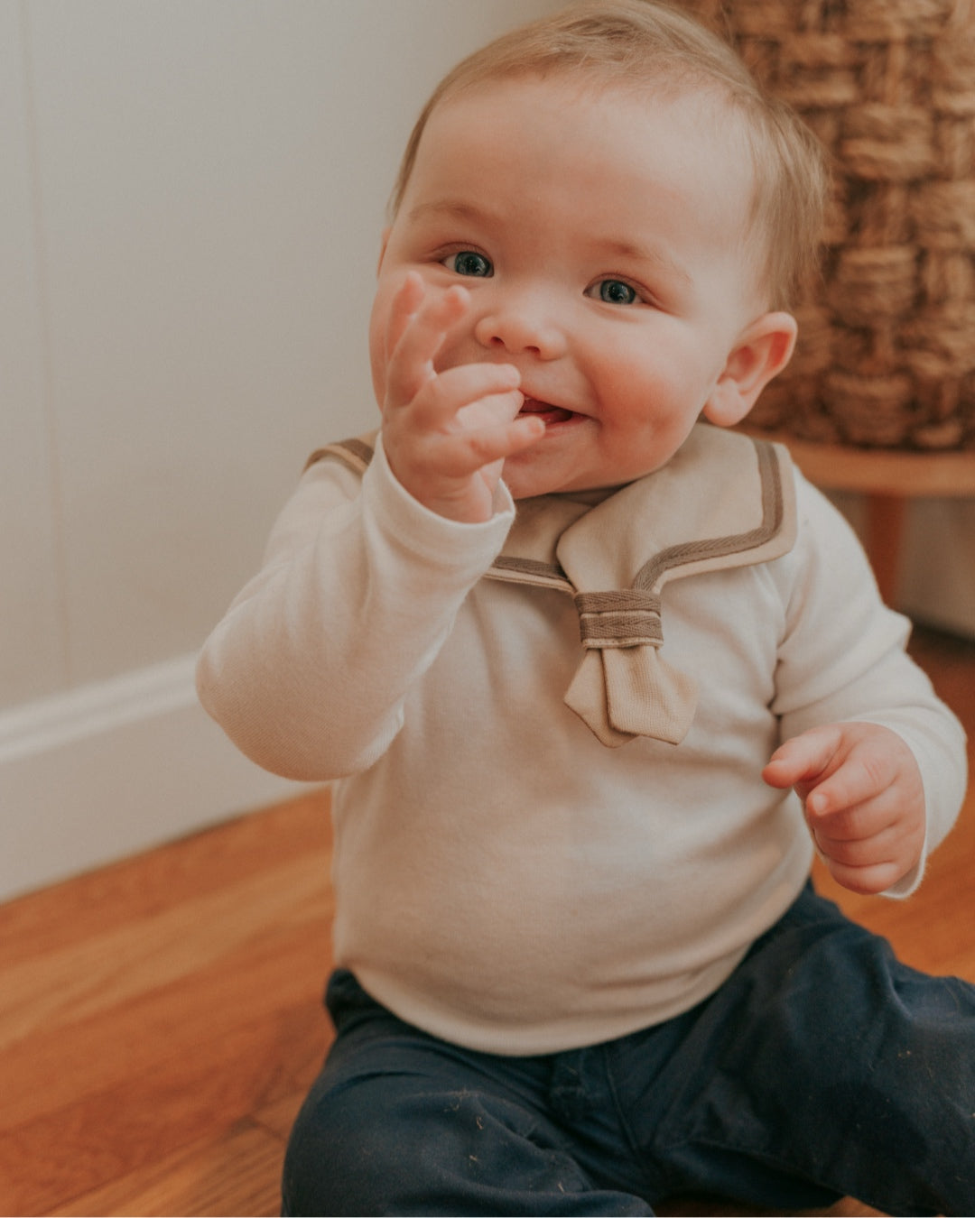 A baby wearing a brown sailor-style collar bib with a knotted tie.