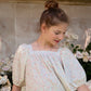 Woman in a floral dress standing among flowers with a neutral background