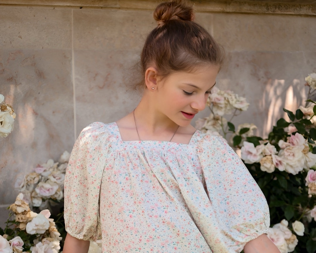 Woman in a floral dress standing among flowers with a neutral background