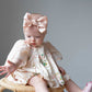Baby sitting on a small stool wearing a floral dress and pink shoes with a large bow headband.
