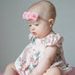 Baby wearing a floral Bubble and headband sitting on a pink surface with a gray background