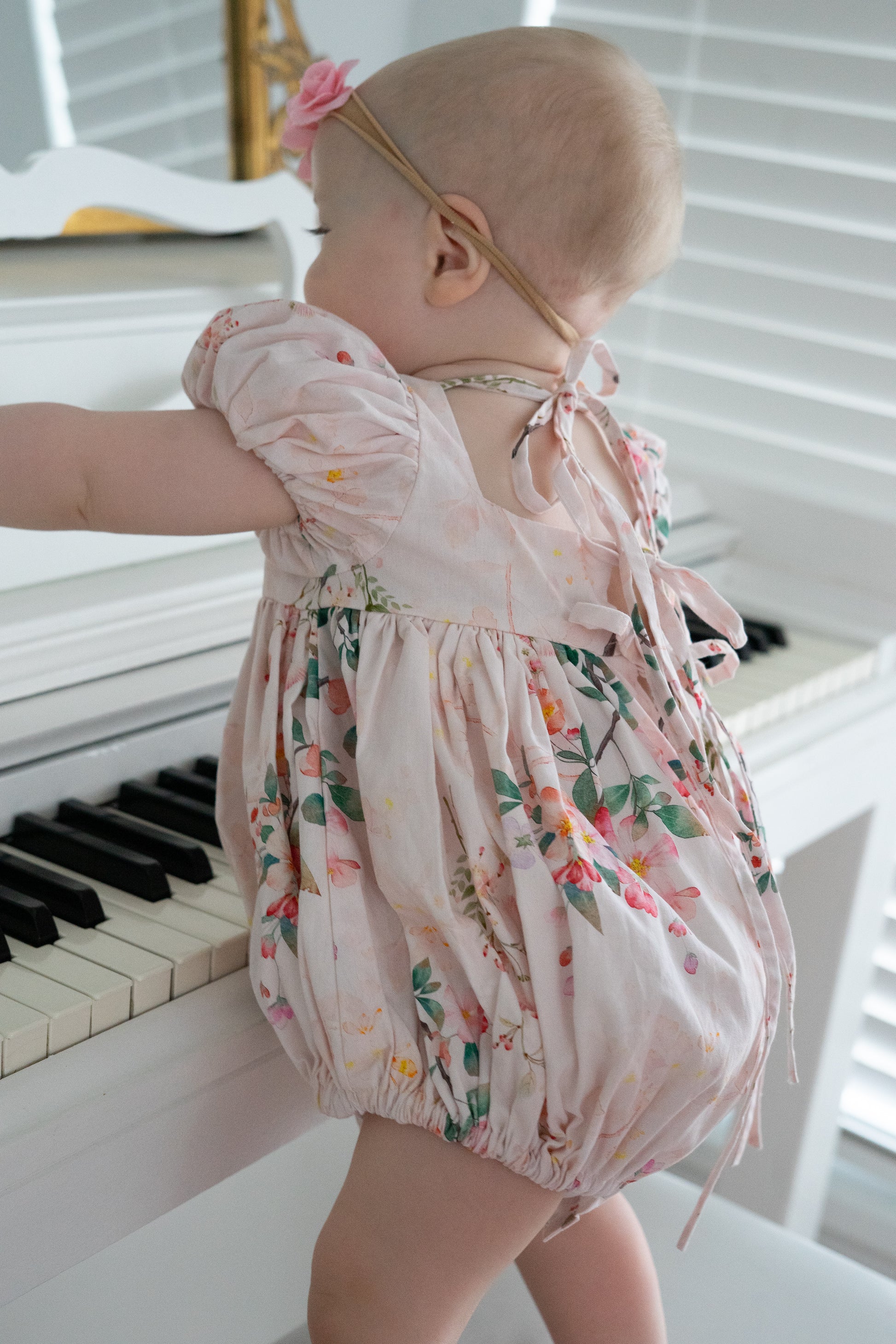 Baby in a floral bubble standing in front of a piano