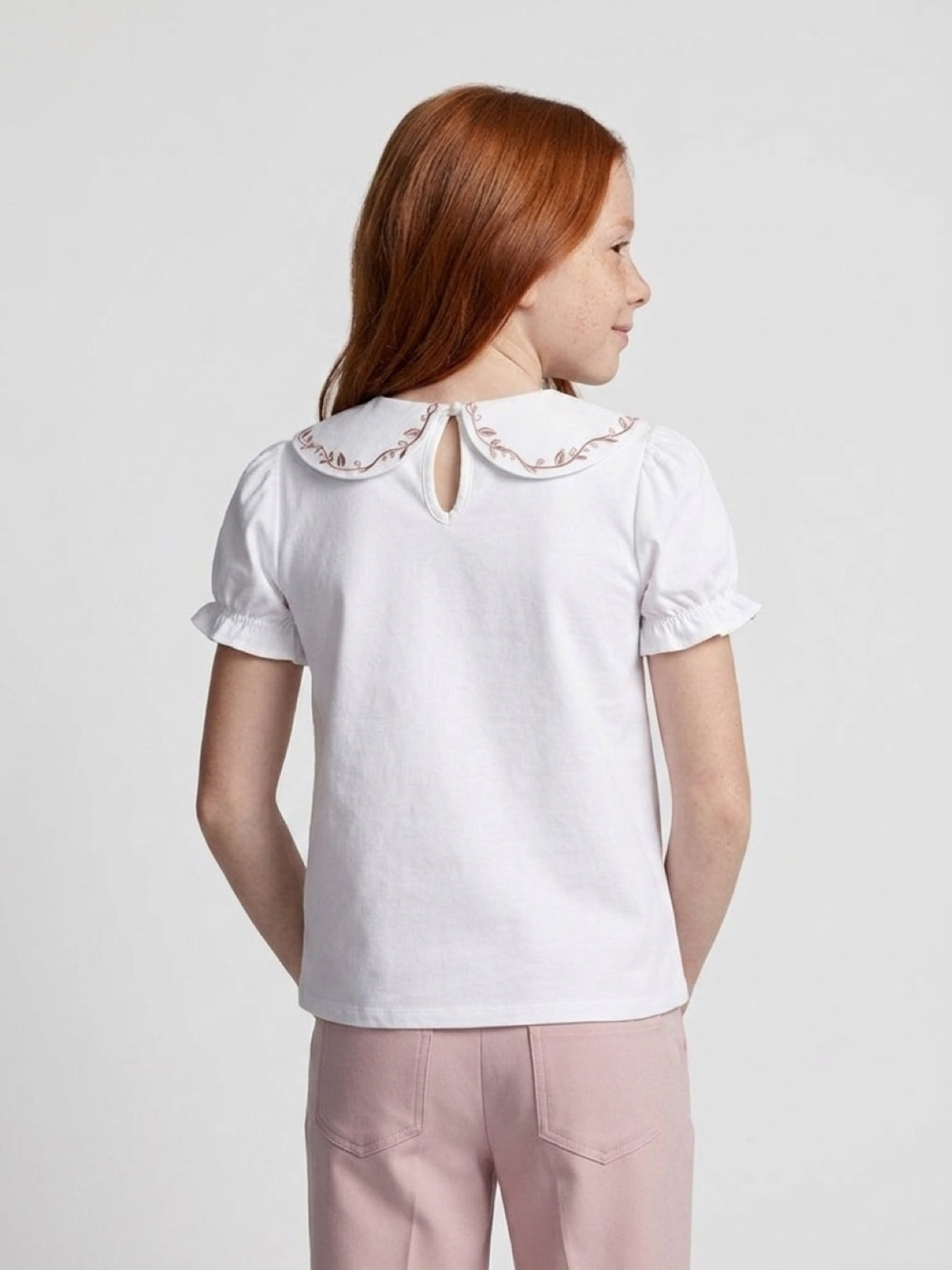 Woman wearing a white blouse with embroidered details on a plain background
