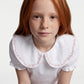 Young girl wearing a white blouse with an embroidered collar on a plain background