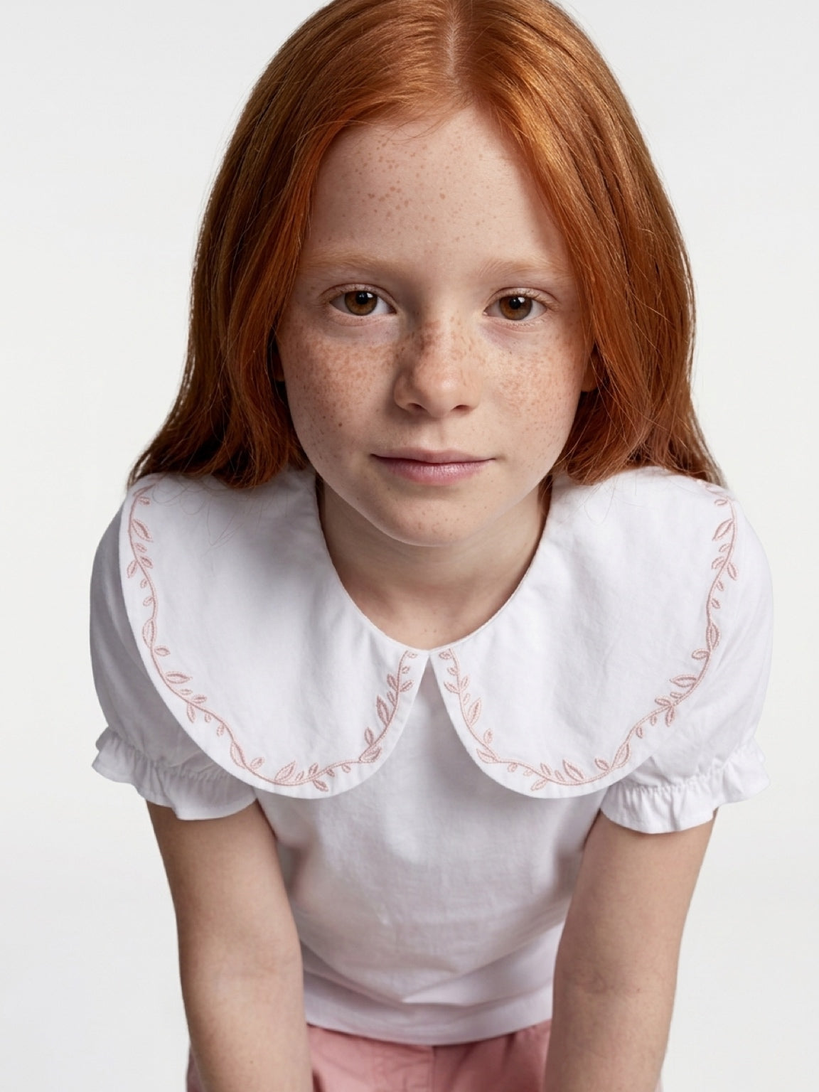 Young girl wearing a white blouse with an embroidered collar on a plain background