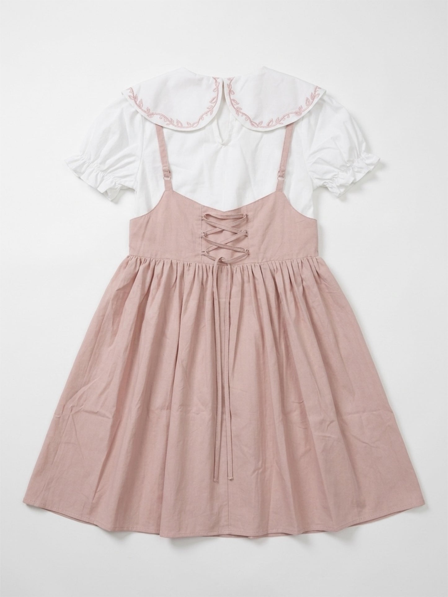 Pink dress with lace-up front and white ruffled top on a light gray background
