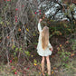 Person in a white dress standing in an apple orchard with bare trees and fallen apples.