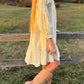 Person wearing a light dress and beige boots standing near a wooden fence in an outdoor setting.