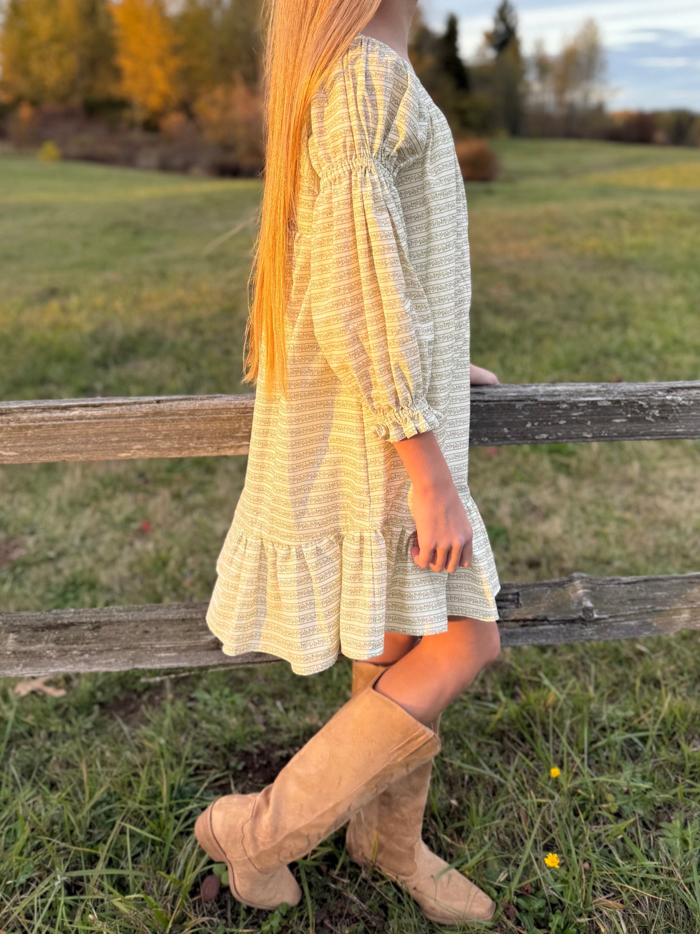 Person wearing a light dress and beige boots standing near a wooden fence in an outdoor setting.