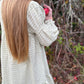 Person wearing a textured dress holding an apple in a natural setting with trees and berries.