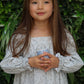 Young girl in a light dress holding a small object against a green leafy background