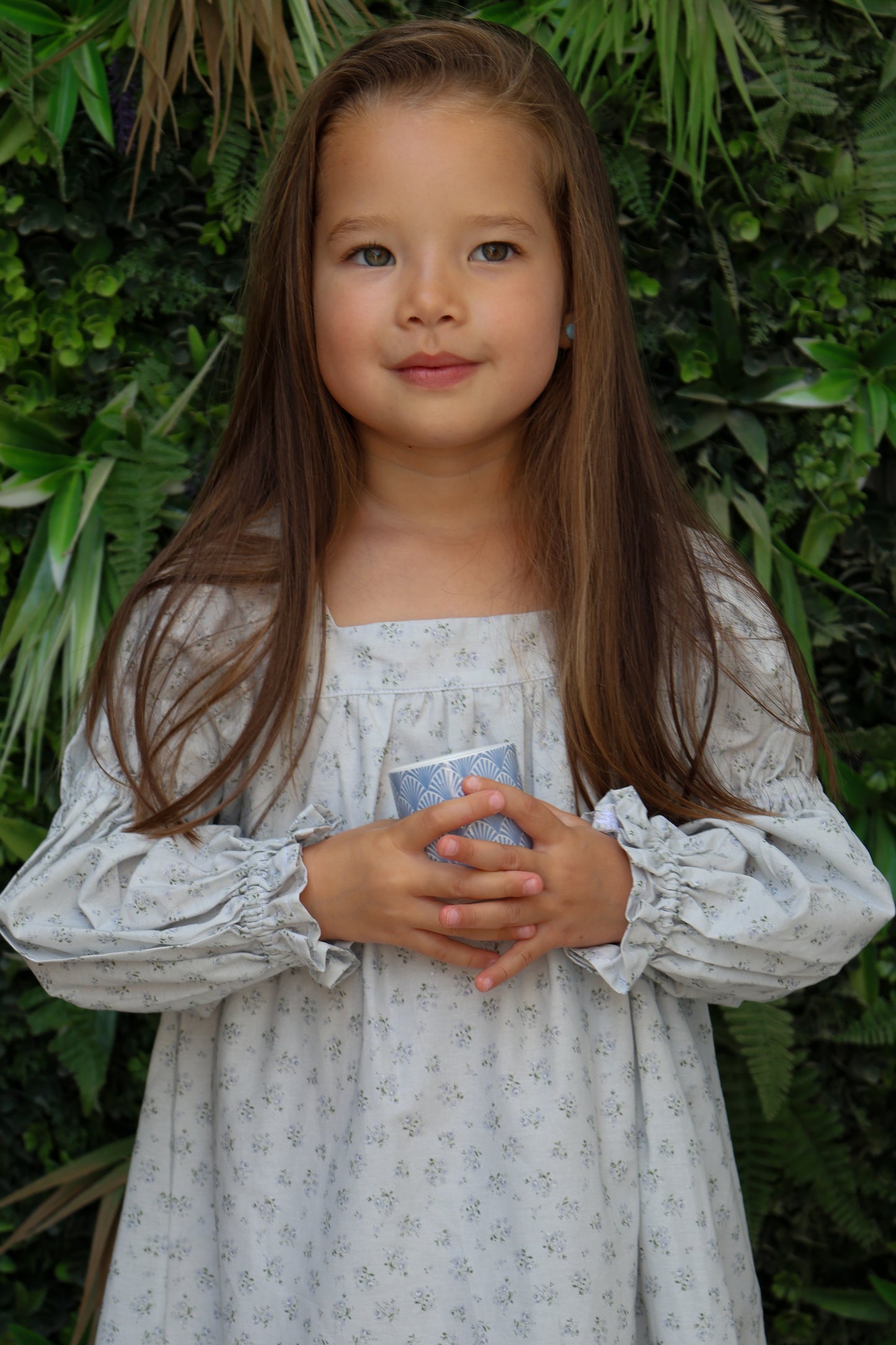Young girl in a light dress holding a small object against a green leafy background