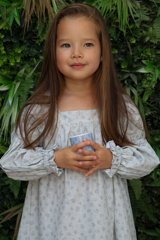 Young girl in a light dress holding a small object against a green leafy background