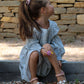 Young girl in a light dress sitting against a stone wall.
