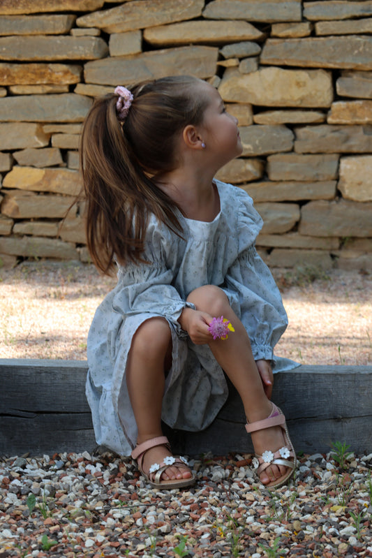 Young girl in a light dress sitting against a stone wall.