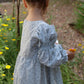 Child in a light blue dress standing in a garden with flowers.